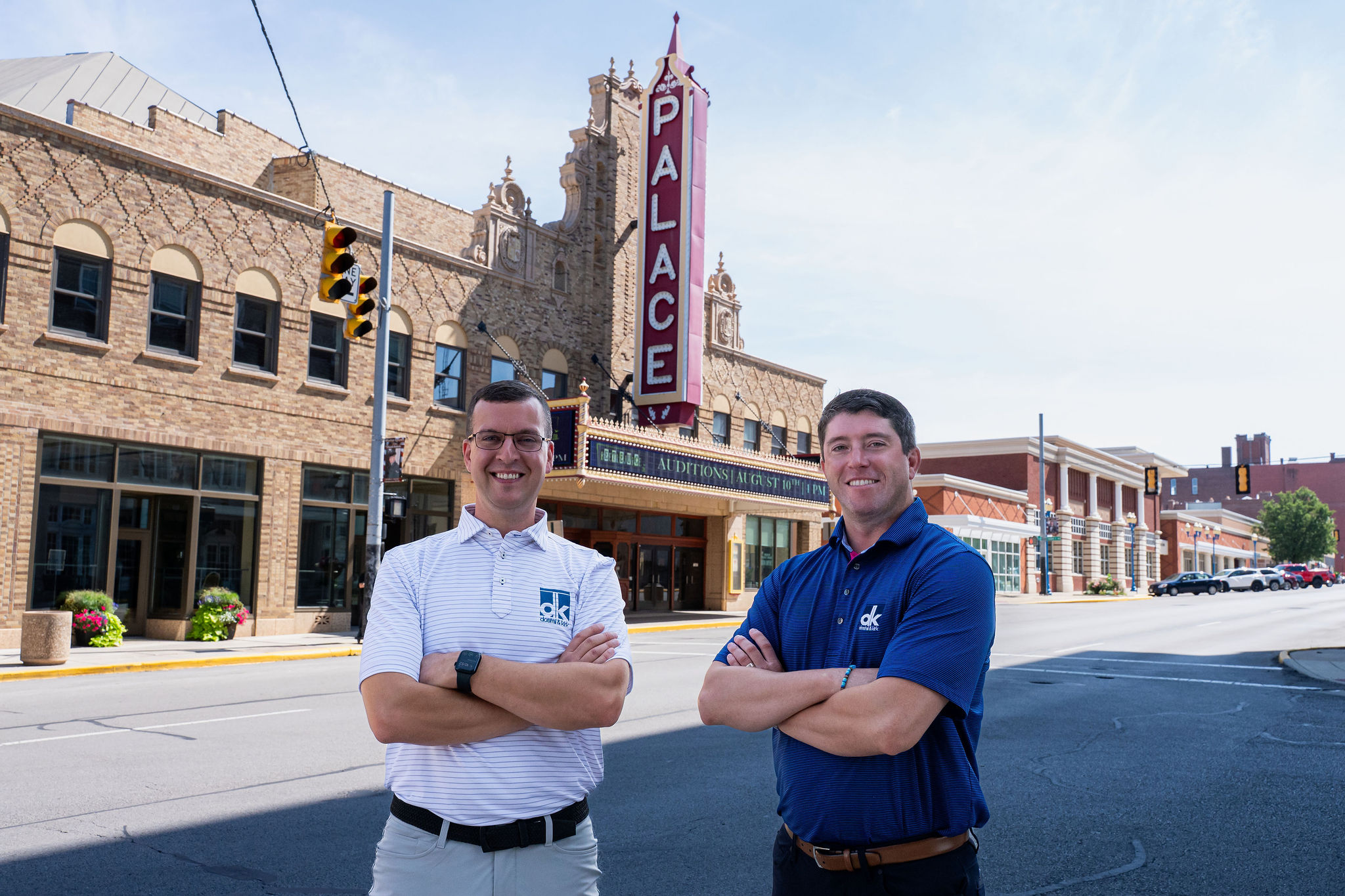 Two Dostal & Kirk team members standing confidently in front of the historic Palace Theatre, representing reliable property and casualty insurance services